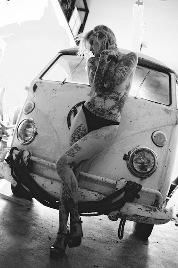 A tattooed babe posing next to a VW bus.