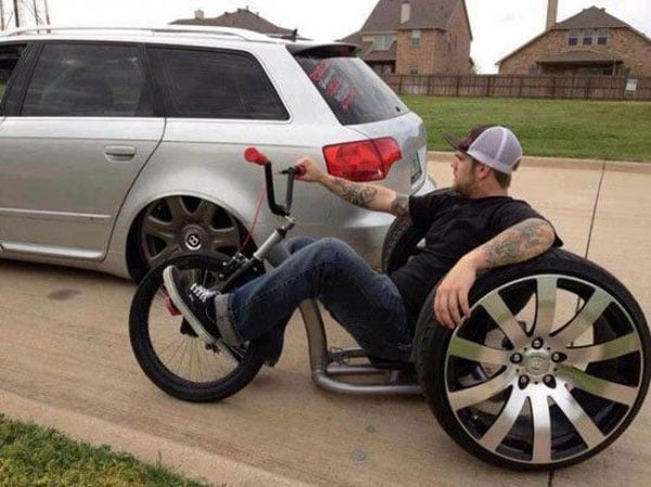 A man on a bike beside a car, contemplating his wants and needs.