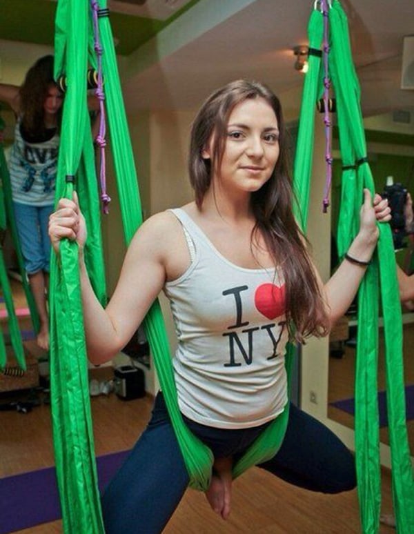 A woman is lounging on a comfy green hammock in a gym, seemingly lost in thought as she relaxes.