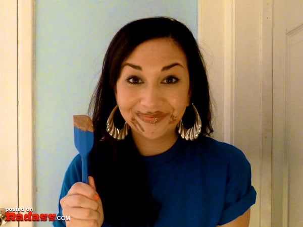 A woman in a blue shirt holding a blue spatula, expressing