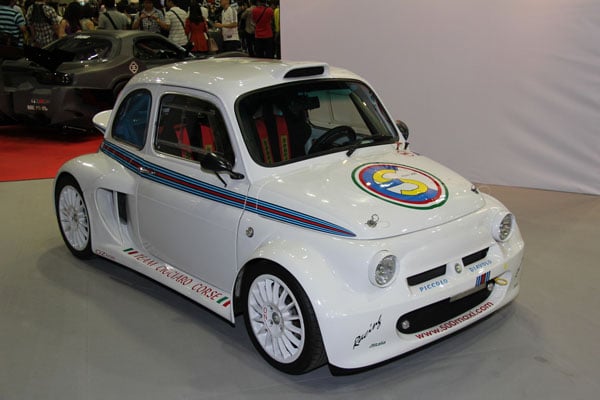 A small white car is on display at a Just Cool Ass Cars & Trucks show.