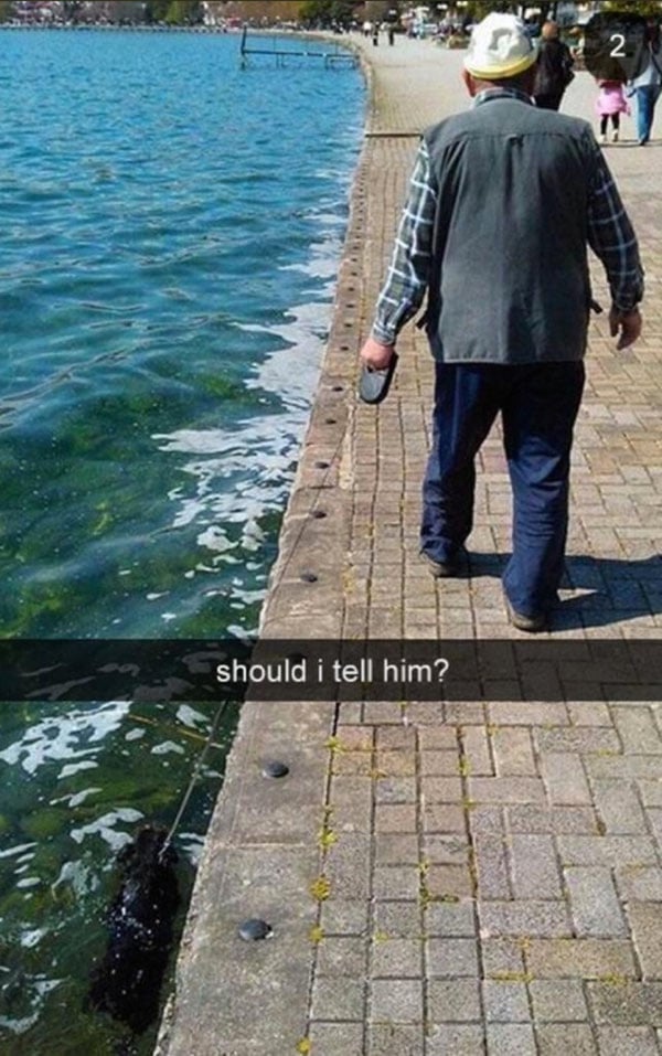 An old man captures funny Snapchats while walking his dog near the water.
