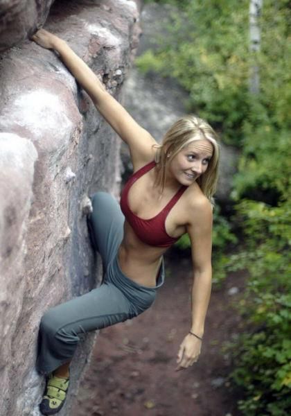 A woman is parkouring on a rock in the woods.