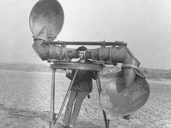 A man standing next to a large speaker in the sand, reminiscing about 11 Jobs That No Longer Exist.