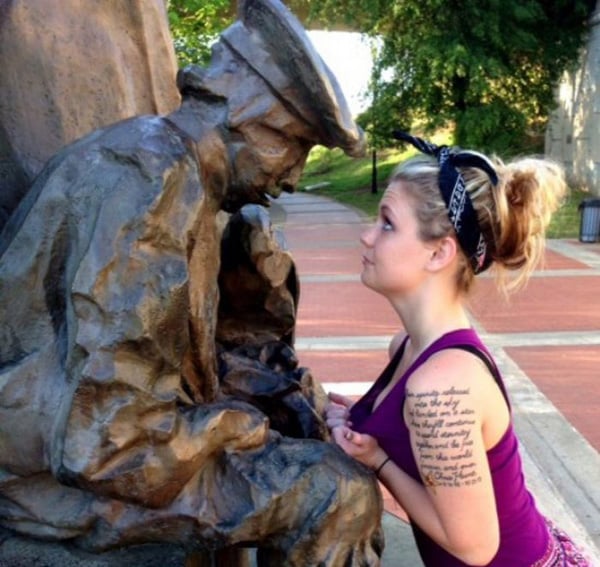 A woman kneeling next to a statue of a man, contemplating the words