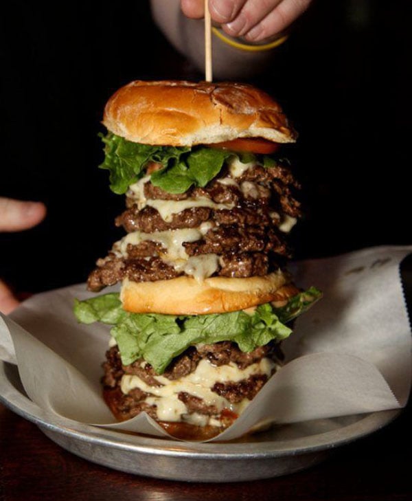 A person holding a large burger on a plate with wants vs. needs in mind.