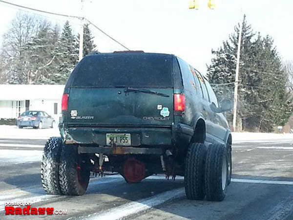 A snowy road traveled by a green SUV.