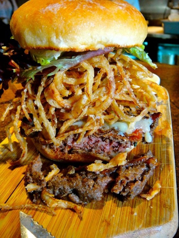 An awesome visual of a large burger on a wooden cutting board, perfect for Super Bowl.