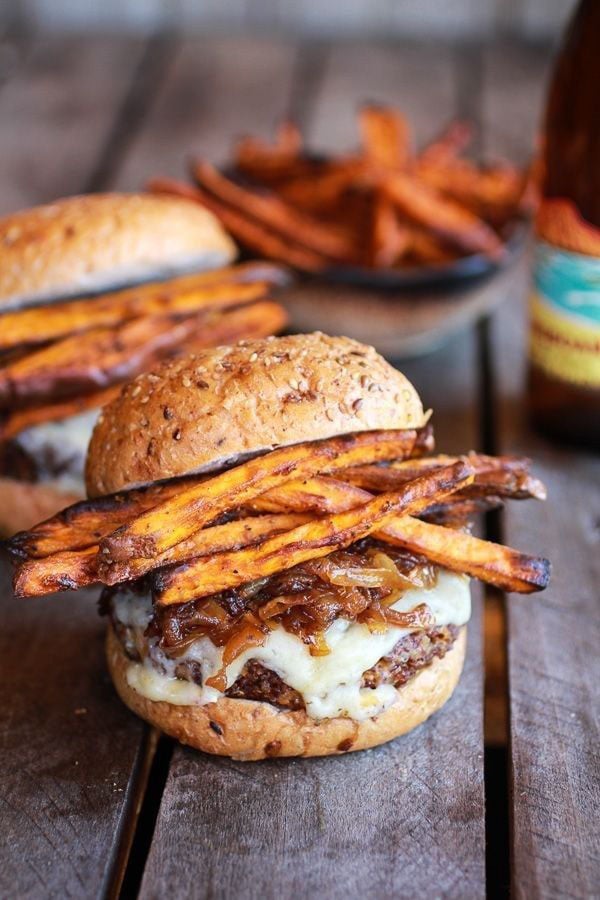 An amazing burger paired with sweet potato fries and a beer, showcased on a rustic wooden table.