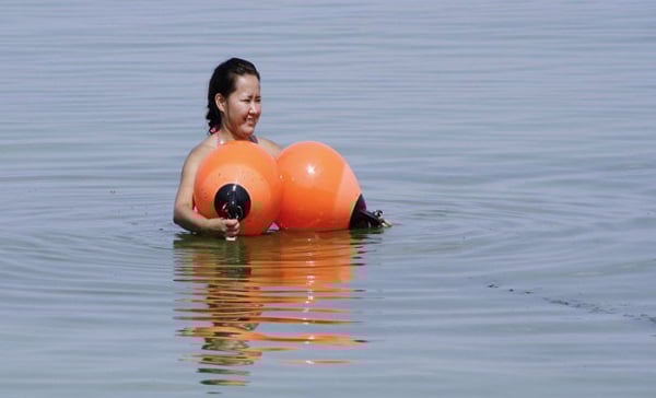 A woman is floating in the water with an orange float, contemplating