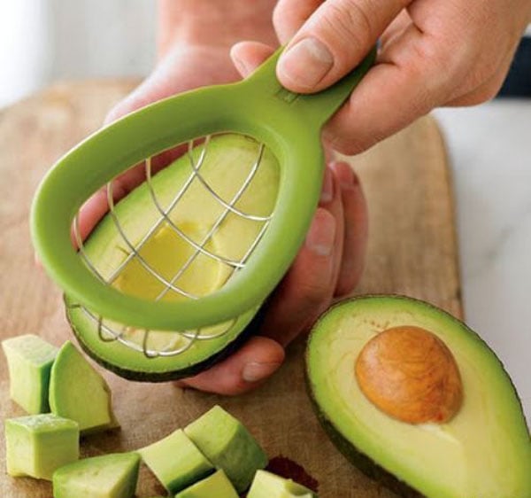 A person using an avocado slicer to cut their avocado.