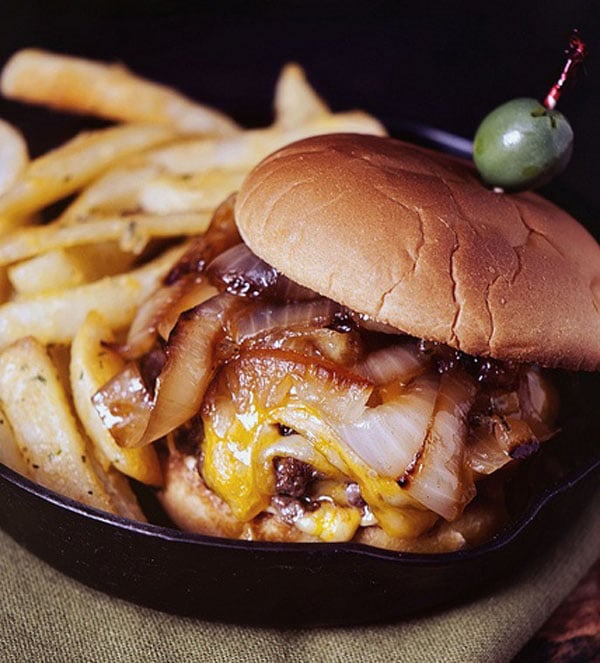An visually appealing Super Bowl burger with fries and onions cooked in a cast iron skillet.