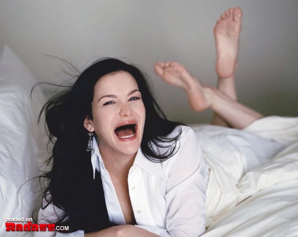 Toothless woman lounging on a bed with her mouth open.