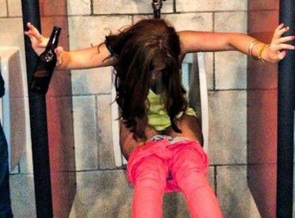 A woman is hanging from a urinal with a beer bottle in this humorous image titled