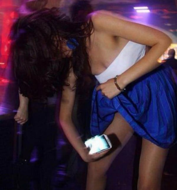 A woman in a blue dress is holding a cell phone, pondering