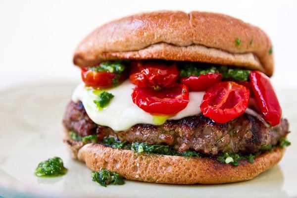 A visually appealing Super Bowl burger with tomatoes and pesto on a plate.