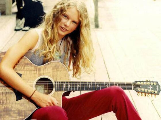 A young woman, one of the famous artists before making the big time, sitting on a wooden deck with an acoustic guitar.