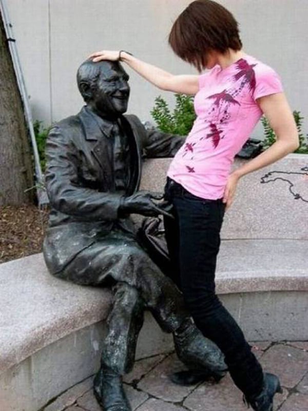 A woman is posing next to a statue of an old man, symbolizing her dilemma of