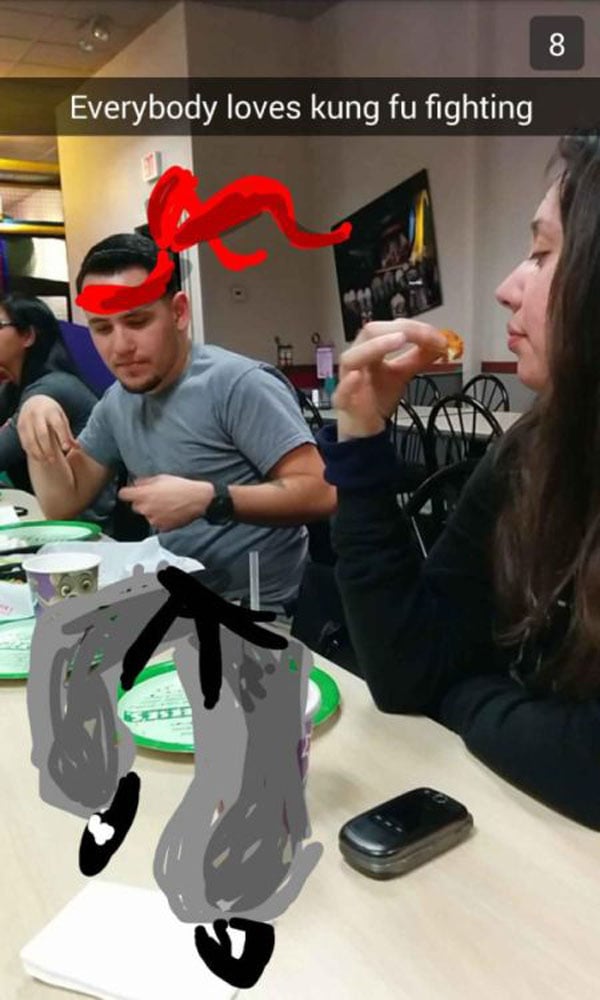 A group of people enjoying funny Snapchat moments while sitting at a table eating food.