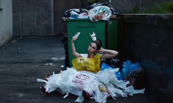A woman sitting on the ground next to a trash can, contemplating