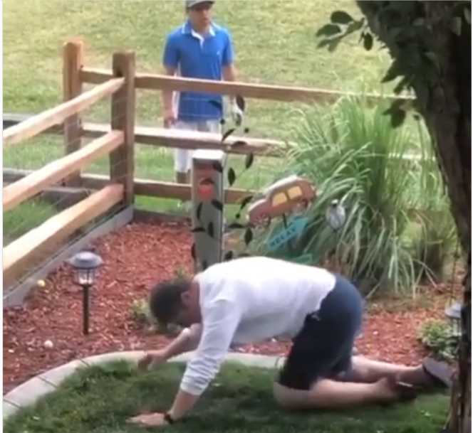 A man is kneeling down in front of a fence.