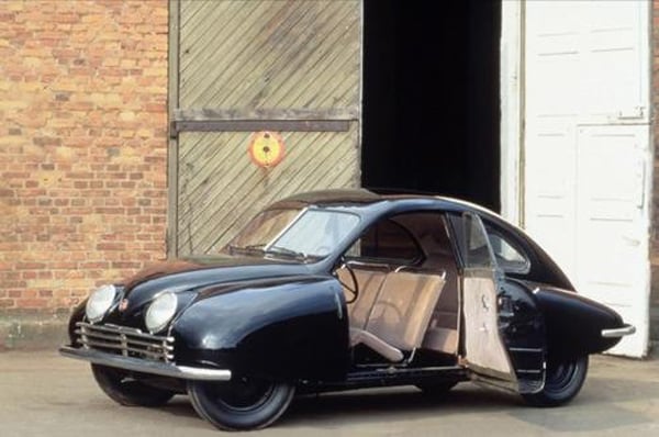 A cool black car with its door open parked in front of a garage.