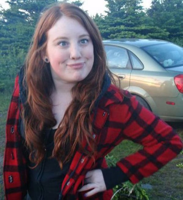 A young woman in a plaid jacket standing in front of a car, wondering