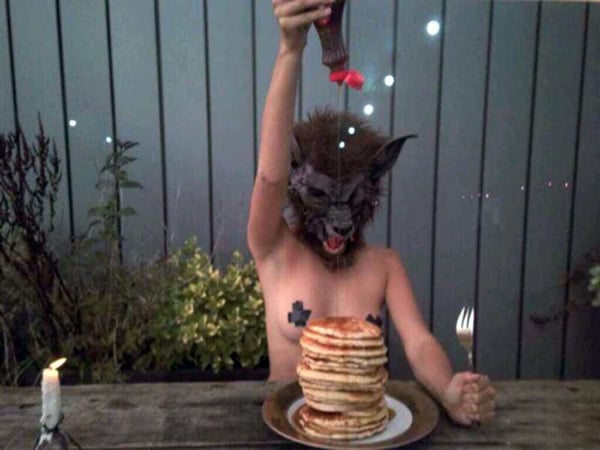 A woman with a wolf mask holding a plate of pancakes while saying,