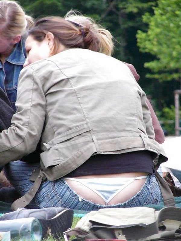 A woman sitting on the grass with her back to the camera, revealing a slight glimpse of her whale tail.