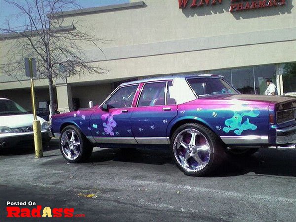 A purple and blue car parked in front of a store, unnoticed.
