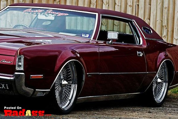 A maroon car parked in front of a fence, unnoticed.
