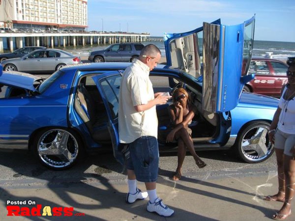 A group of people standing next to a blue car, wondering if they will notice me.