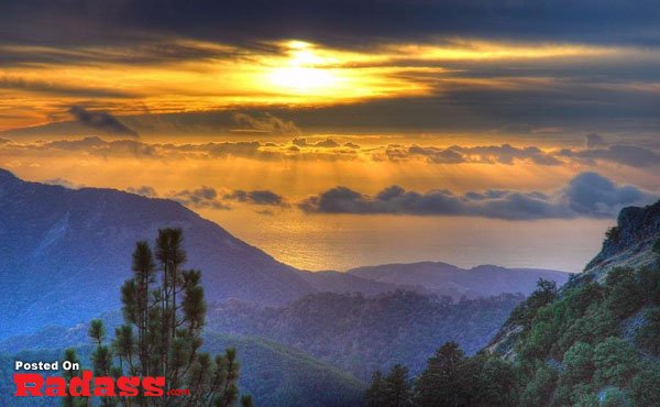 The sun is setting over a mountain with clouds in the background, creating a serene and picturesque scene.