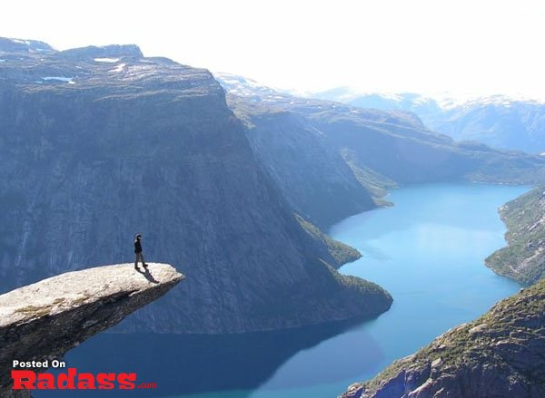 A man on a cliff overlooking a lake, embracing the serene beauty.