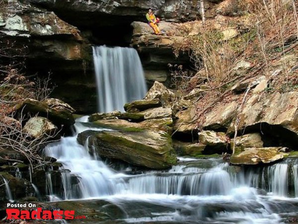 A man stands peacefully in front of a majestic waterfall.