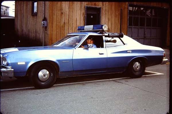 A blue police car is parked in front of a building during the Macy's Day Parade.
