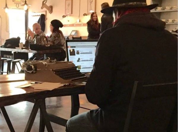 A hipster sitting at a table with a typewriter.