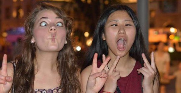 Two girls make a peace sign in front of a crowd.