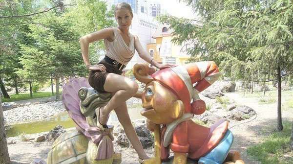 A woman is posing next to a statue of a teddy bear.