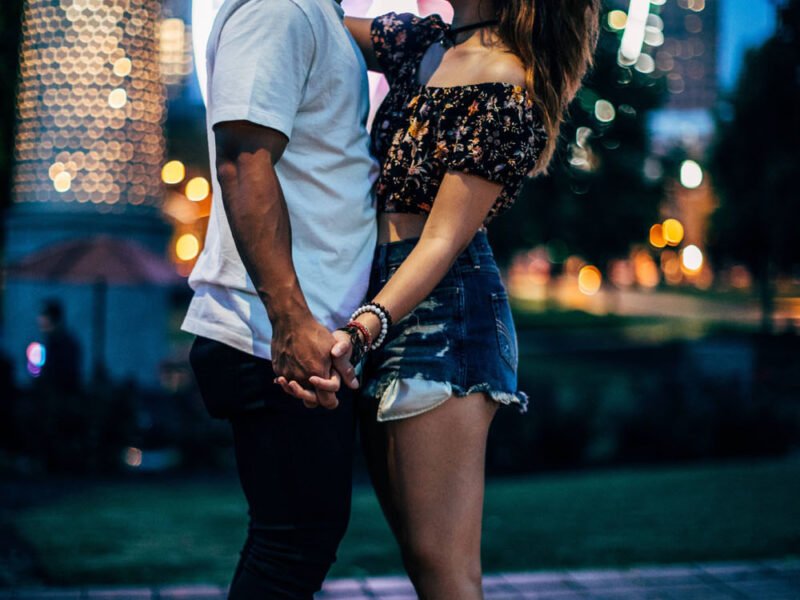 A couple sharing a tender kiss in front of a majestic ferris wheel on a Saturday morning, capturing cool pics of their love and happiness.