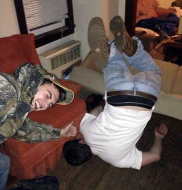 A man is doing a flip on a couch in a living room and face plants.