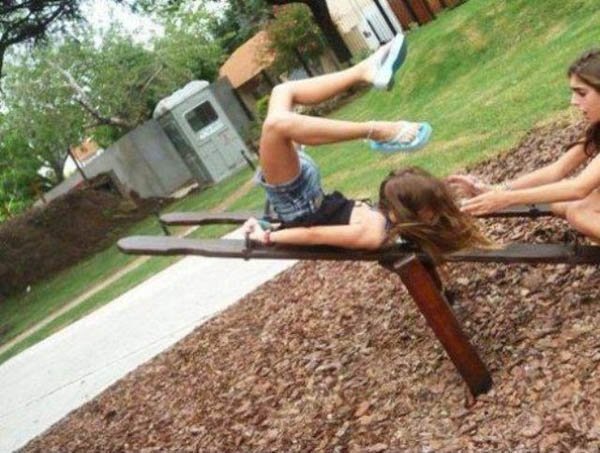 Two girls laying on a wooden bench in a park, face planting.