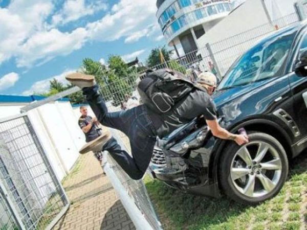 A man face plants while jumping on top of a car in front of a fence.
