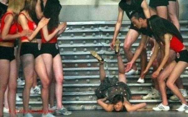 A group of people on a stage with a woman who face plants on the floor.