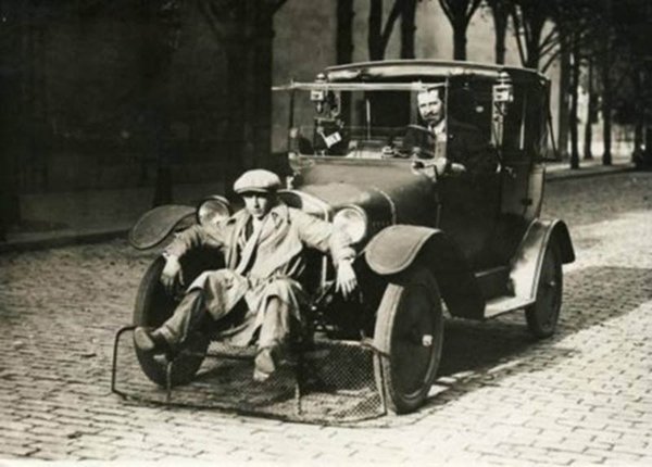 An old photo of a man sitting in a car from the early 1900's.