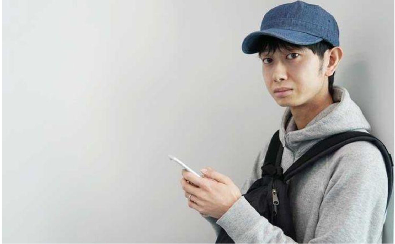 A young man with a hat and backpack, absorbed in his phone.