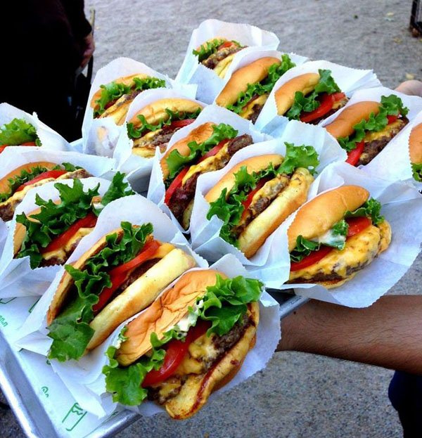 A man is holding several sandwiches on a tray, offering a delicious food experience.