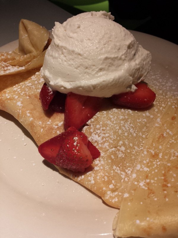 A plate of indulgent crepes oozing with whipped cream and adorned with fresh strawberries - a feast for food porn enthusiasts.