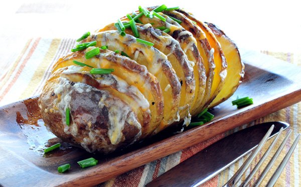 A food porn-worthy roasted potato adorned with chives on a rustic wooden plate.