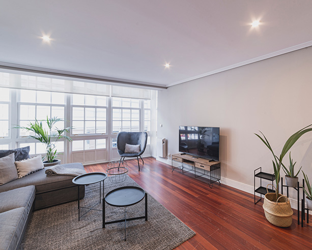 calle-real-92-2-07 Salón luminoso con sofá en L, televisión y ventanales en apartamento de alquiler en A Coruña